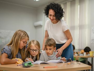 Teacher helping three children with their schoolwork in a classroom.