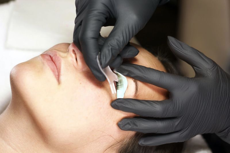 Close-up of a woman getting eyelash extensions by a beautician. Using tweezers, the extensions are applied to her natural lashes. Her eyes closed in relaxation during the painless two-hour procedure.