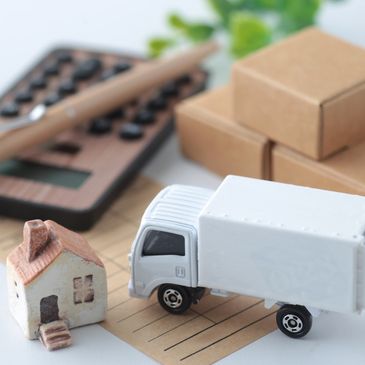 Miniature house and delivery truck with calculator and boxes in background.