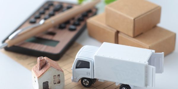 Miniature house and delivery truck with calculator and boxes in background.