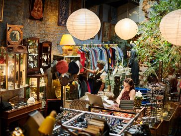 A cozy vintage store with two women browsing and working amid warm lighting.