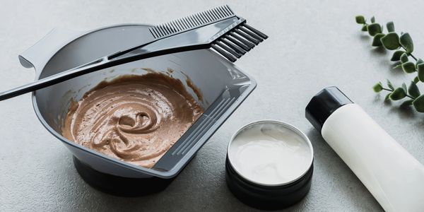 Hair dyeing tools with brown hair color mixture on a gray surface.