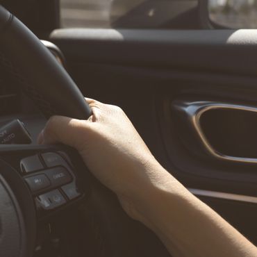 A hand gripping a car's steering wheel near control buttons.