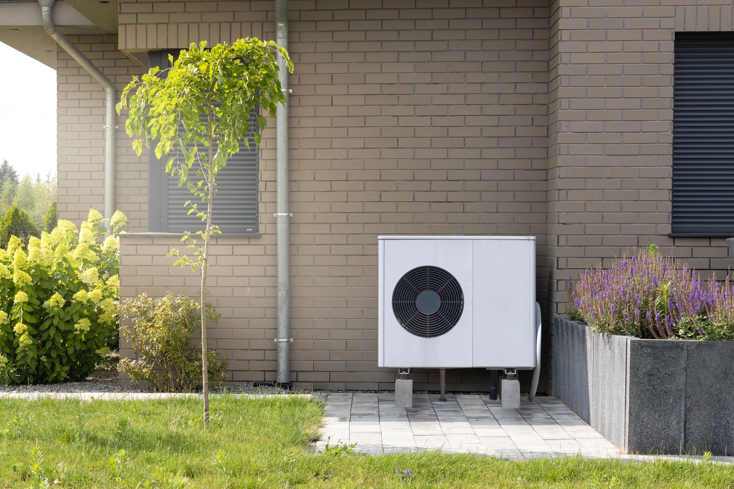 heat pump outdoor unit on elevated stand outside a tan brick house
