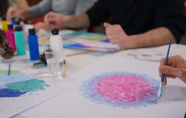 Hands creating colorful fingerprint art on tree drawings.