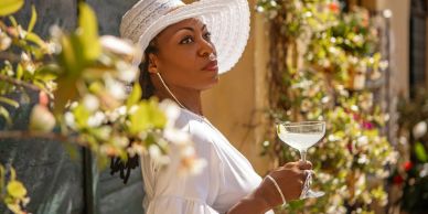 Woman in a white hat holding a glass outdoors.