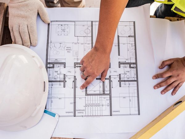 Person pointing at a building blueprint on a table.