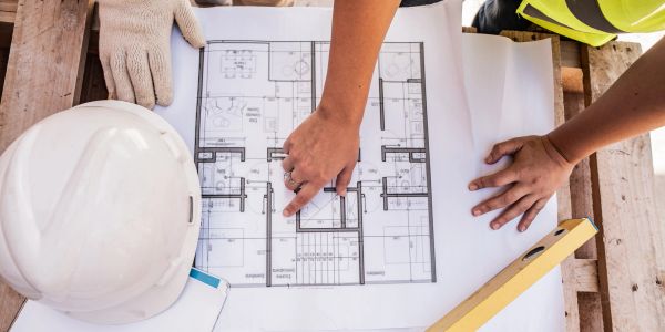Hands pointing at architectural blueprints on a construction site table.