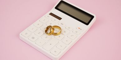Two gold wedding rings on a white calculator against a pink background.
