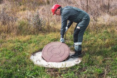 Worker lifting a manhole cover in a grassy field.