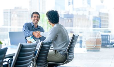 Two men shaking hands at a business meeting in a modern office.