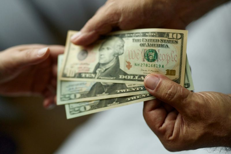Close up of unrecognizable man paying someone with dollars.