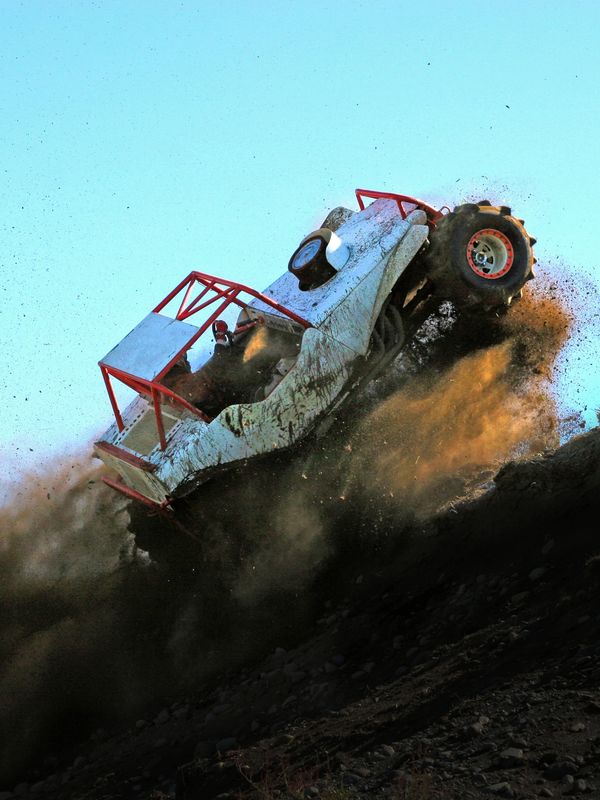 Off-road vehicle climbing steep dirt hill kicking up dust.
