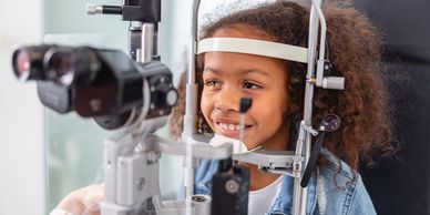 Young girl undergoing an eye exam with a slit lamp at the optometrist.