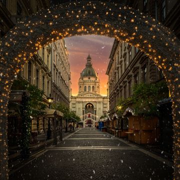 Archway with lights framing a church at sunset with falling snow.