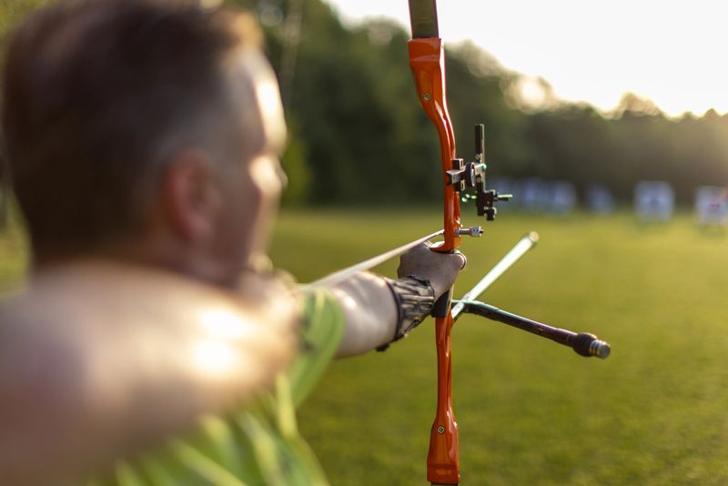 Mid adult man practicing archery. He is holding the bow and aiming at target.