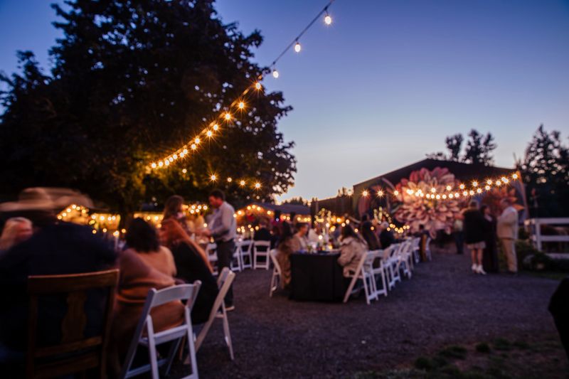 Outdoor Wedding Reception at Night. Long exposure of an outdoor wedding ceremony at twilight and guests having a fun celebrating. Motion blur makes any people unrecognizable. Barn and string lights set the scene for the style.