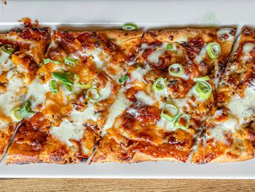 Flatbread pizza with melted cheese, green onions, and sauce on a rectangular plate.
