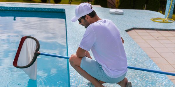 Man cleaning pool with a net while squatting on tiled edge.