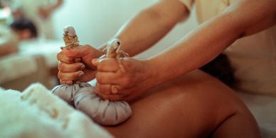 Hands holding herbal compresses for massage therapy.