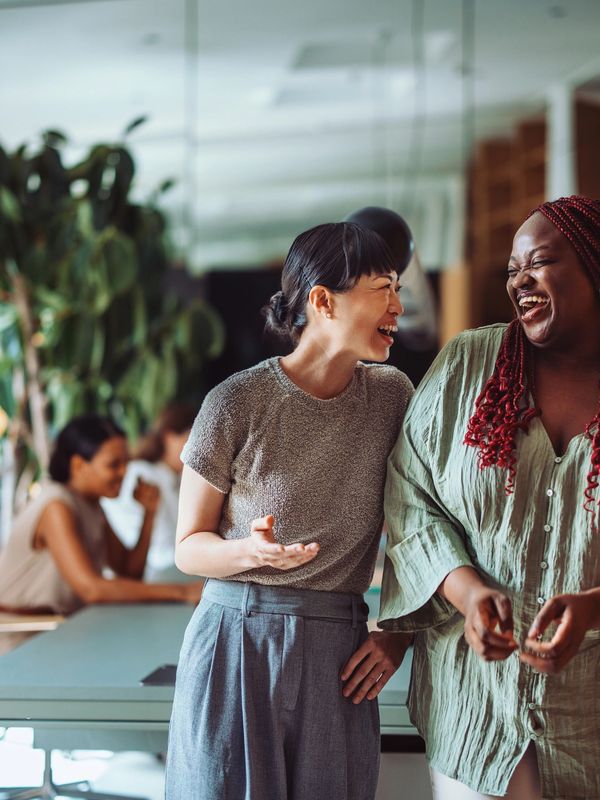 Two women sharing a joyful moment and laughing together in a modern office.