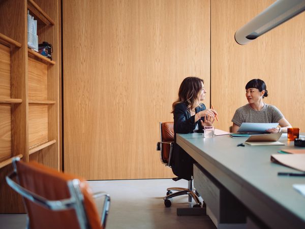 Two women discussing documents in a modern office with wooden walls.
