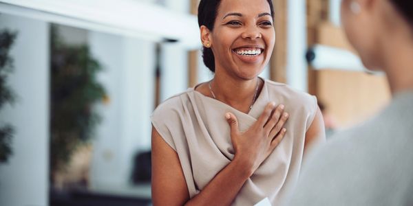 A woman smiles warmly, expressing gratitude with her hand on her chest during a conversation.