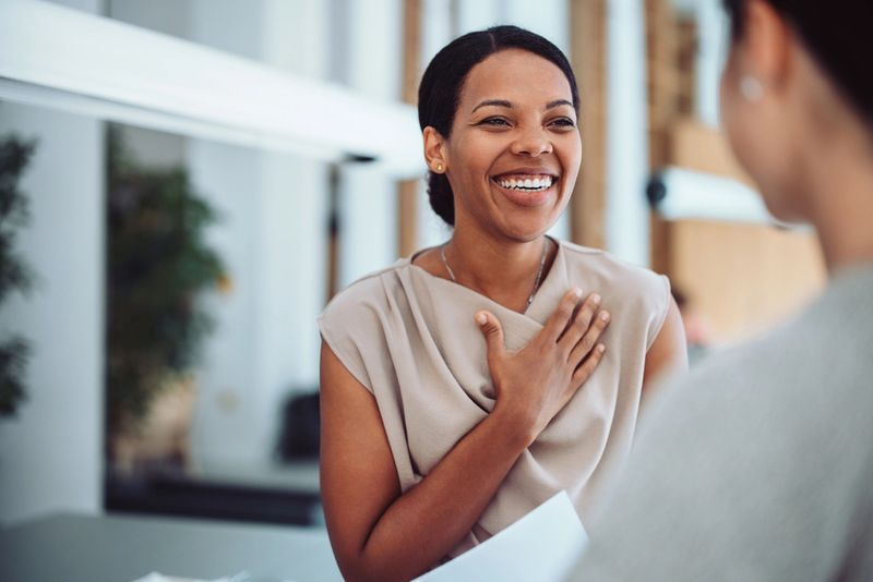 A woman smiles warmly with her hand on her chest, expressing gratitude and happiness during a heartfelt conversation.