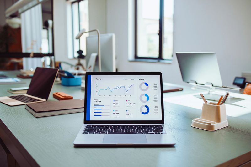 A contemporary office setup featuring laptops and business analytics graphs on screens, representing productivity, data analysis, and modern professional environments.