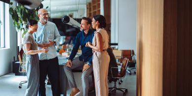 Four coworkers chatting casually in an office setting.