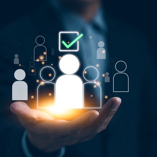 Hand holding glowing people icons with a checkmark above one figure.