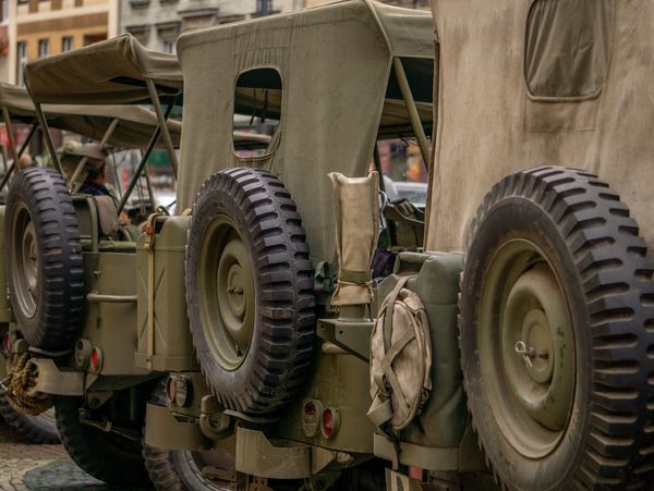 Row of vintage military jeeps with canvas tops and spare tires.