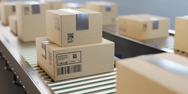 Stacked cardboard boxes with barcodes on a conveyor belt in a warehouse.