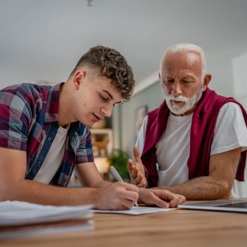 One student teenage caucasian man teen study learn with help of his tutor professor or grandfather senior man at home having private lesson to prepare for exam education concept real people copy space