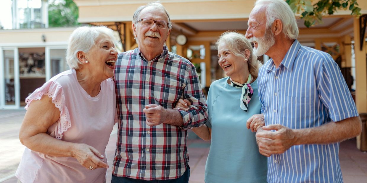Four elderly friends laughing and enjoying each other's company outdoors.