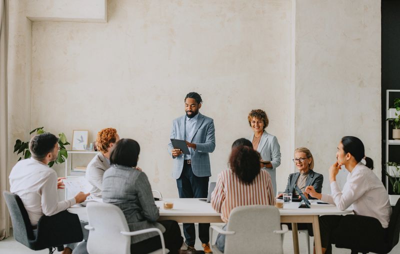 A diverse group of professionals having a business meeting in a bright, modern, beige-colored office. Includes collaborative discussion and teamwork.