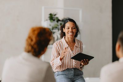 A woman presenting with a tablet to an attentive audience in a modern office.