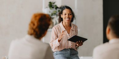Woman speaking to a small group with a notebook.