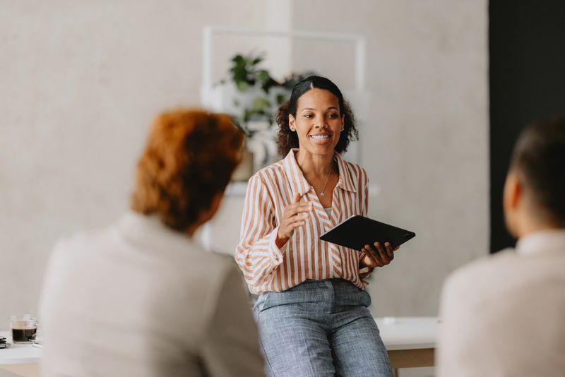 Confident businesswoman leading a group business meeting at a bright beige office. Professional interaction and teamwork concept.