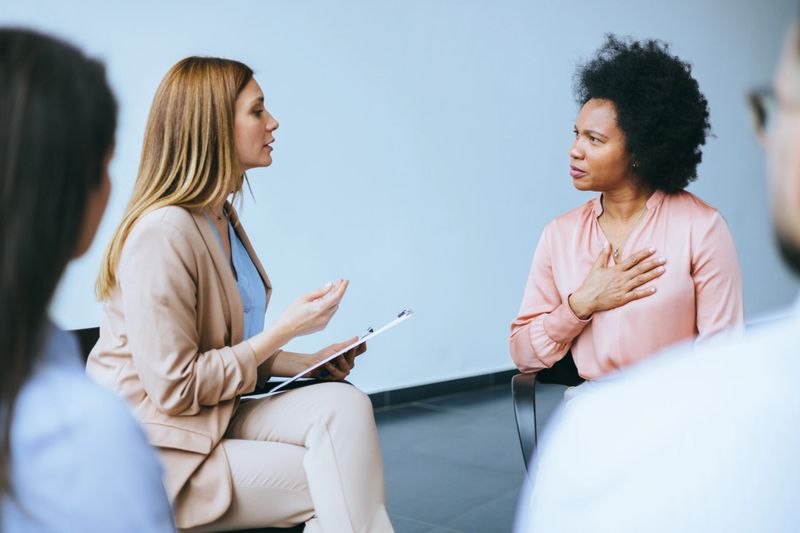 Colleagues engage in a serious professional discussion, with a focus on a female speaker in a meeting room