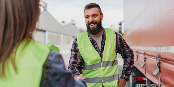 Two workers in reflective vests shaking hands outdoors.
