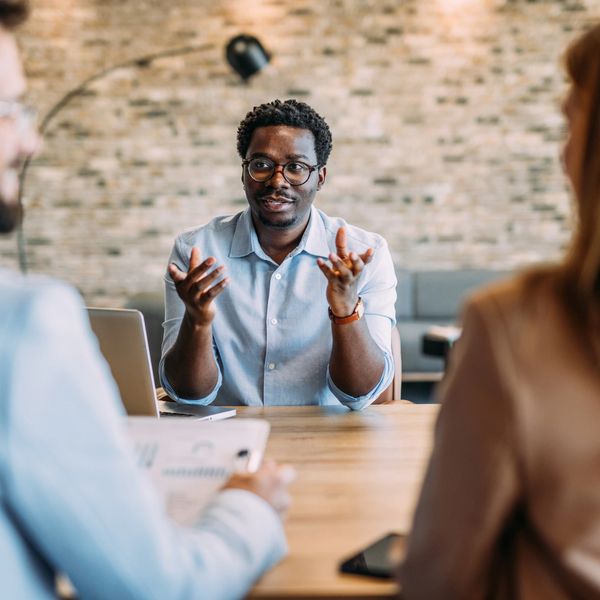 Man in glasses explaining something to two colleagues in a meeting.