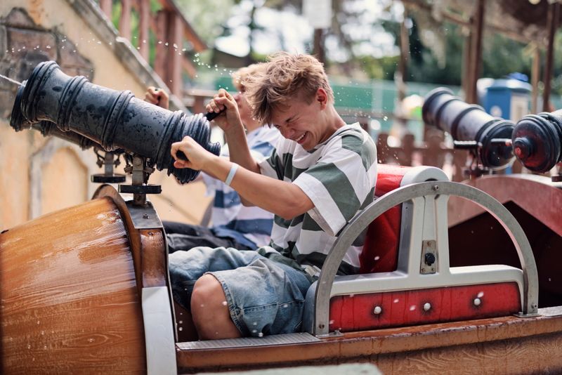 Teenage boys having fun in a water cannon ride in amusement park. Kids are enjoying the ride on a summer day. 
Shot with Canon R5