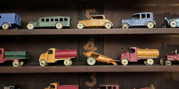 Vintage toy cars and trucks displayed on numbered wooden shelves.