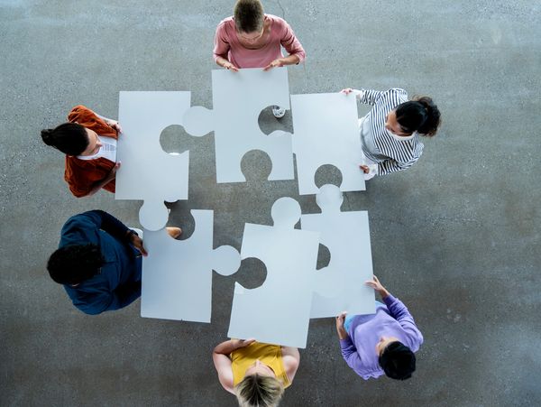 Six people holding large puzzle pieces, viewed from above.