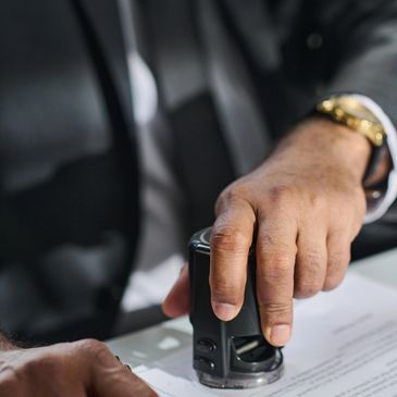 Person in suit stamping a document on a desk.