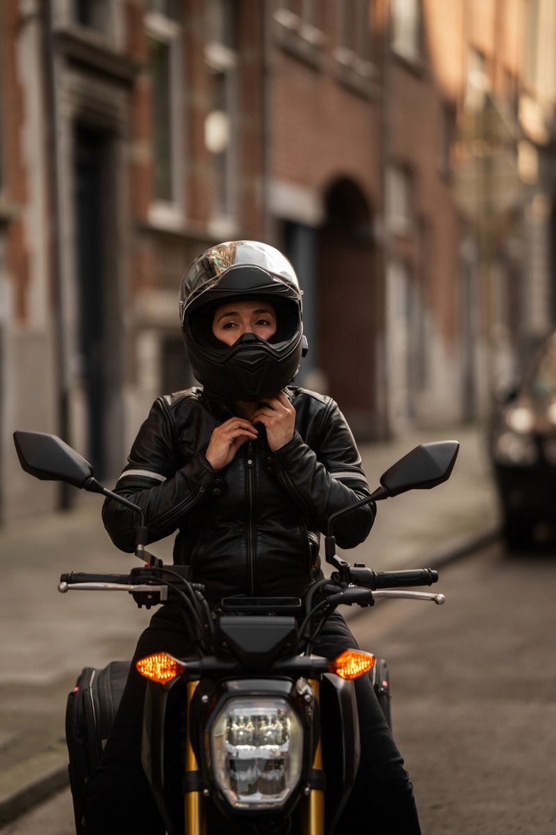 Female biker sitting on motorcycle and putting on helmet while preparing for the ride in the city