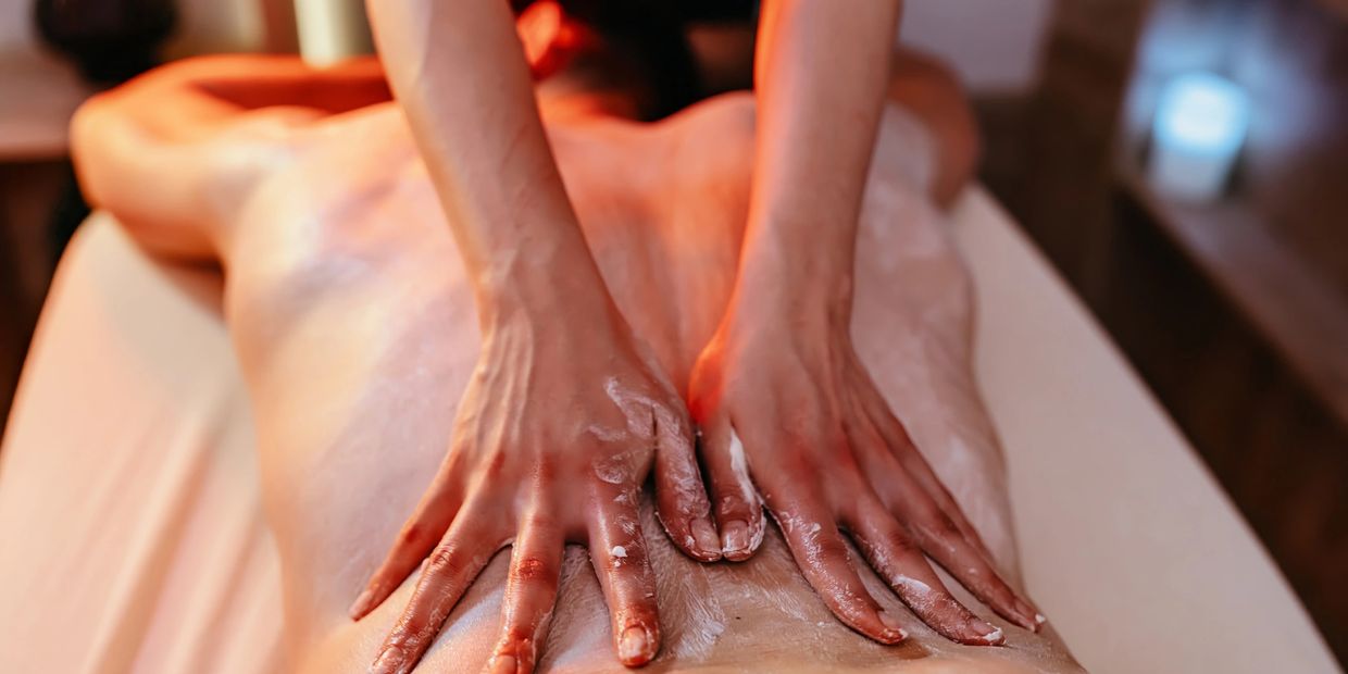 Hands applying massage cream on a person's back in a spa setting.