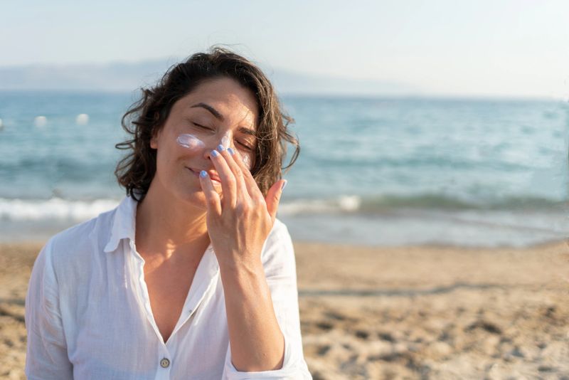 Woman Applying Sunscreen Cream On Her Face At The Beach