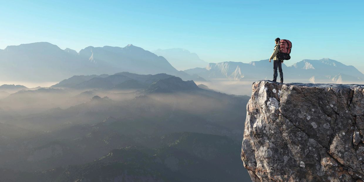 Hiker standing on a cliff overlooking misty mountains at sunrise.